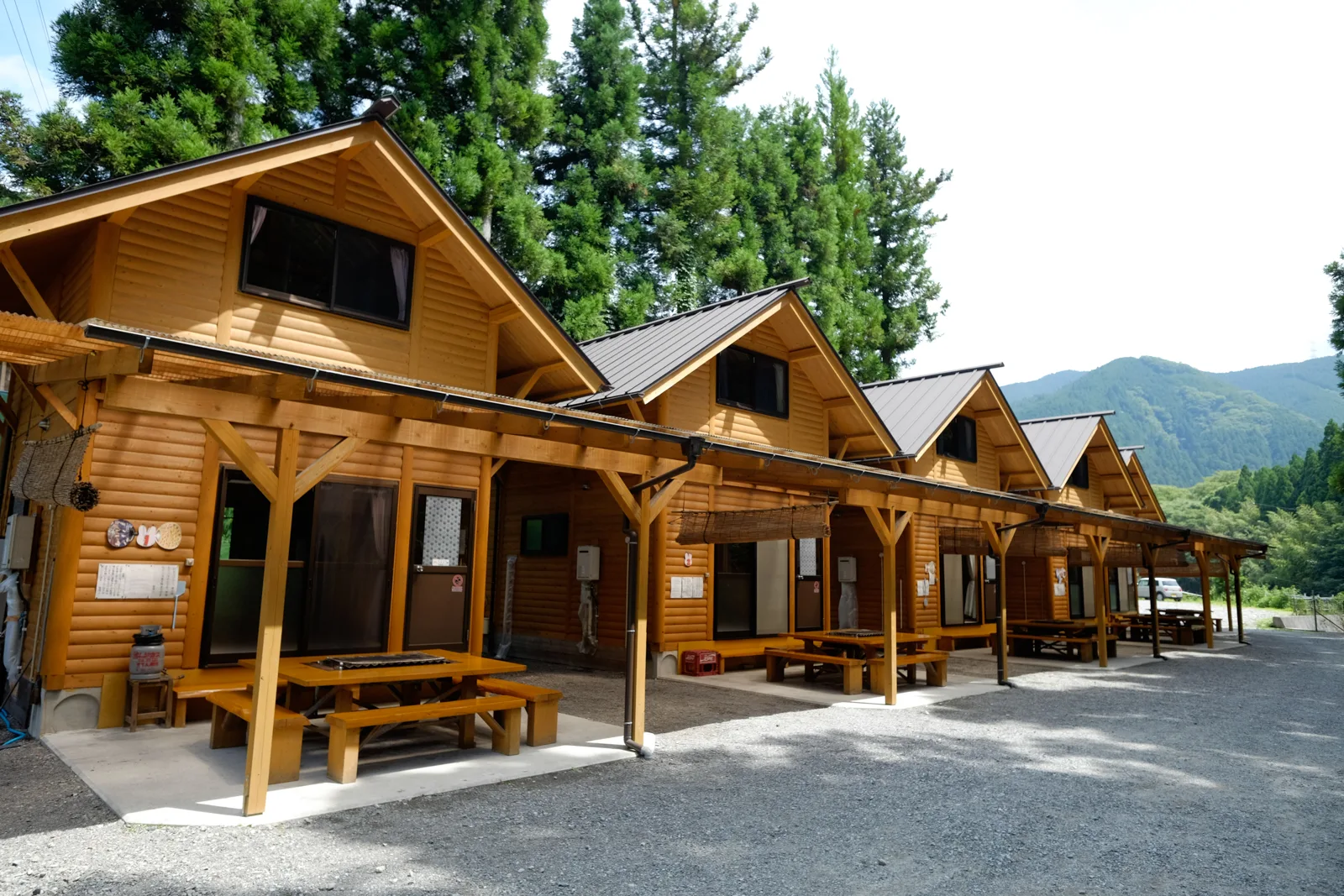テラス席のついたログハウスが並ぶ。うしろは杉木立と山
